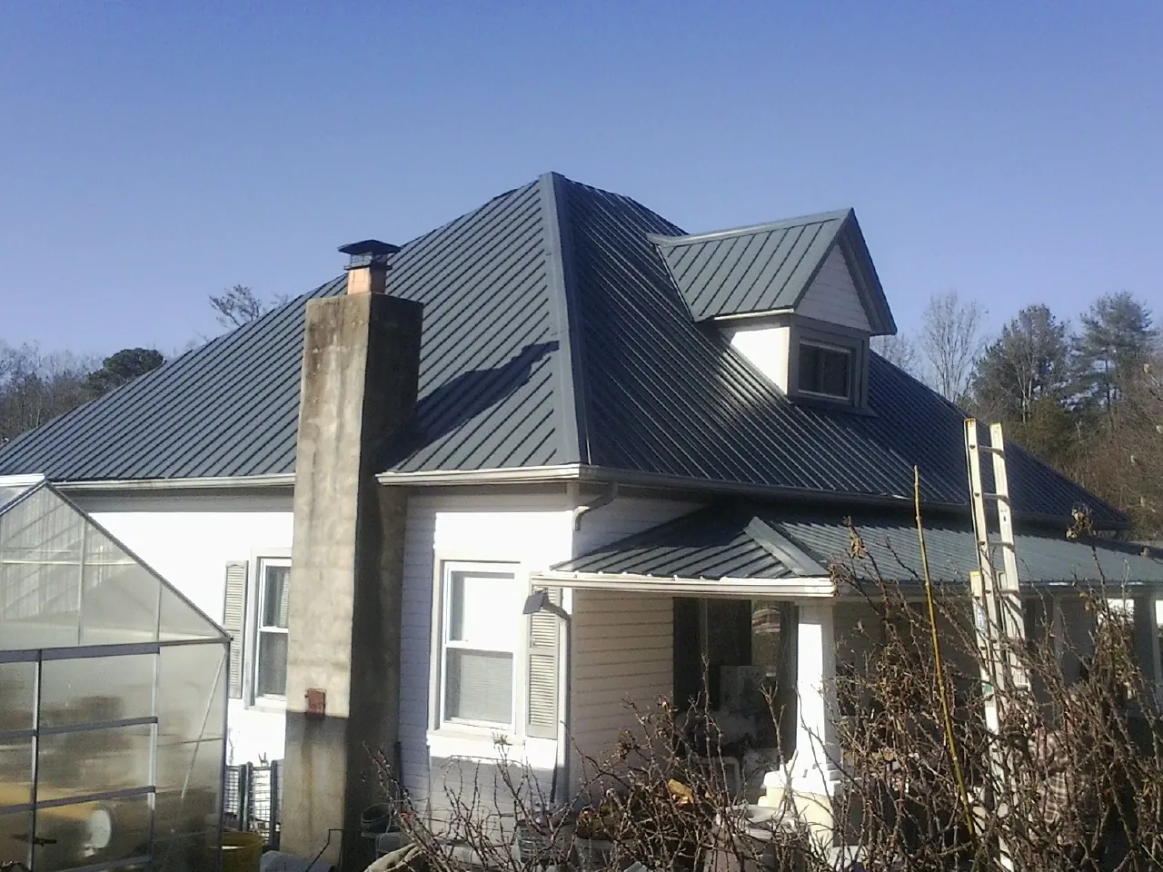 Dark blue standing seam metal roof on a white farmhouse with dormer — Slate & Tile Roof Repair by Roofing Brothers in Empire