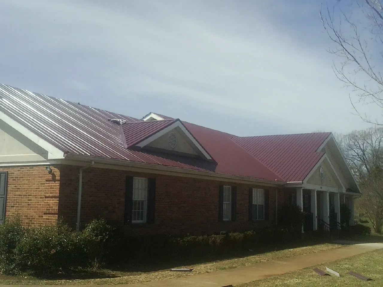 Red metal roof with gabled entries on a long brick building, from a Hail Damage Roof Repair job in Empire