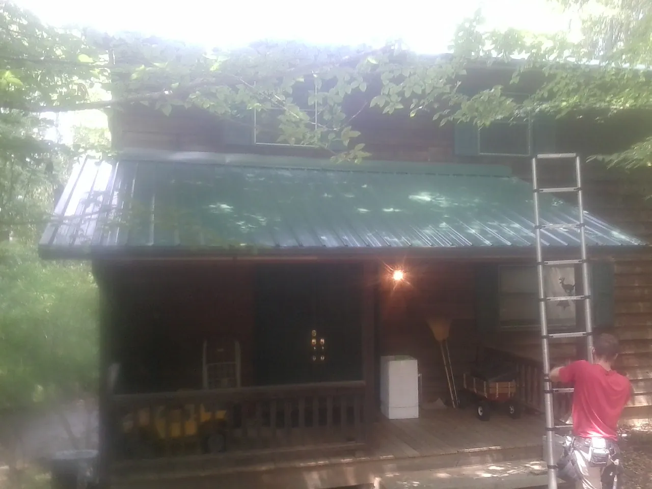 Worker on a ladder at the green porch roof of a wooded cabin in Empire